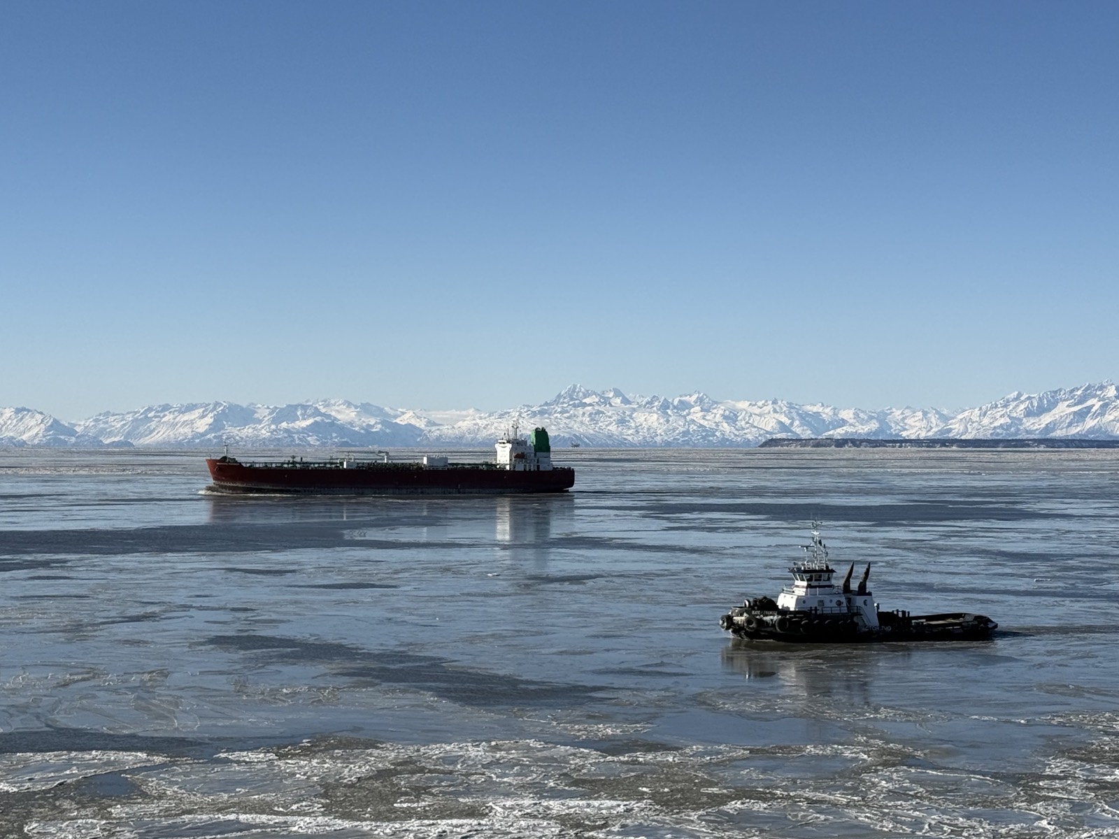 A tanker and tug in the winter ice of Cook Inlet with the Alaska Range beyond
