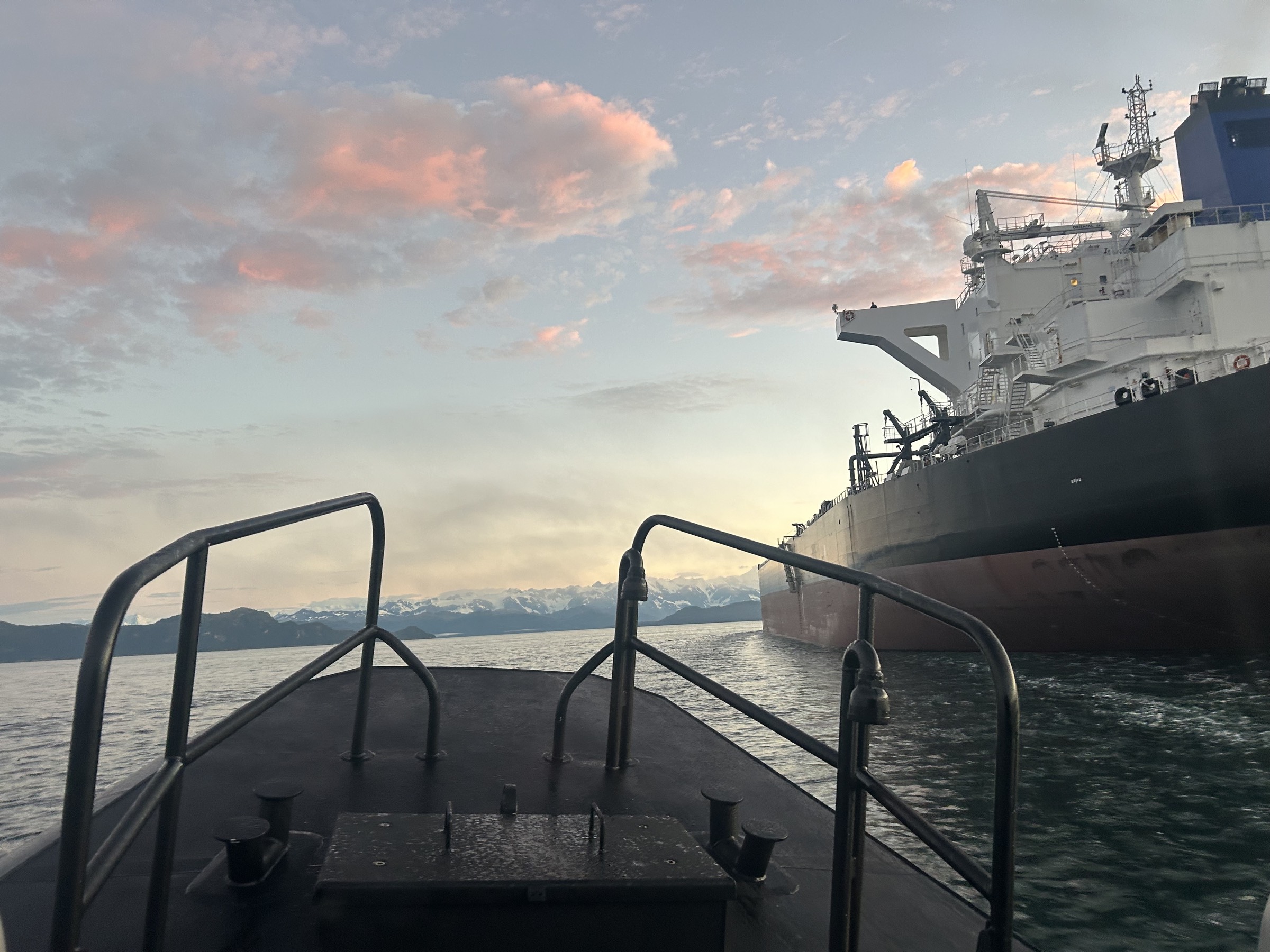 A Southwest Alaska pilot boat running alongside a tanker at dusk, with snow-covered mountains beyond