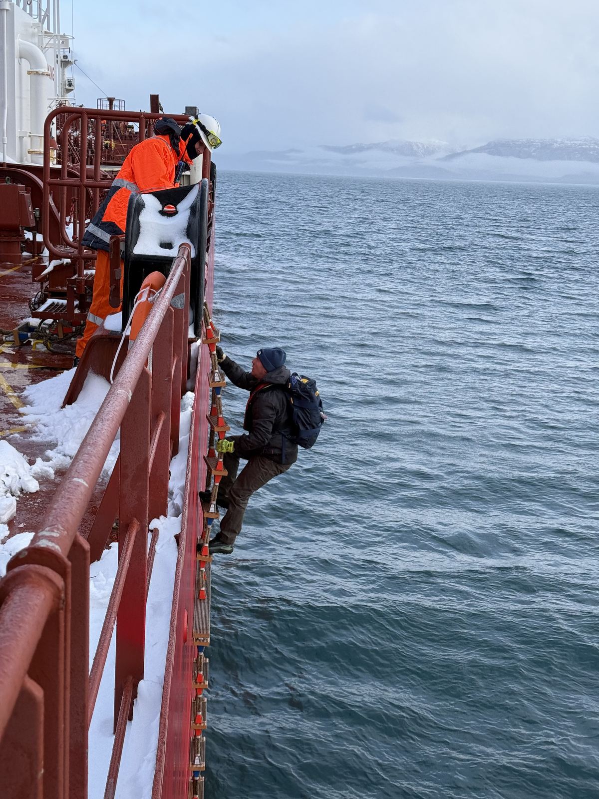 A pilot climbing a pilot ladder from the pilot boat in the snow in Kachemak Bay