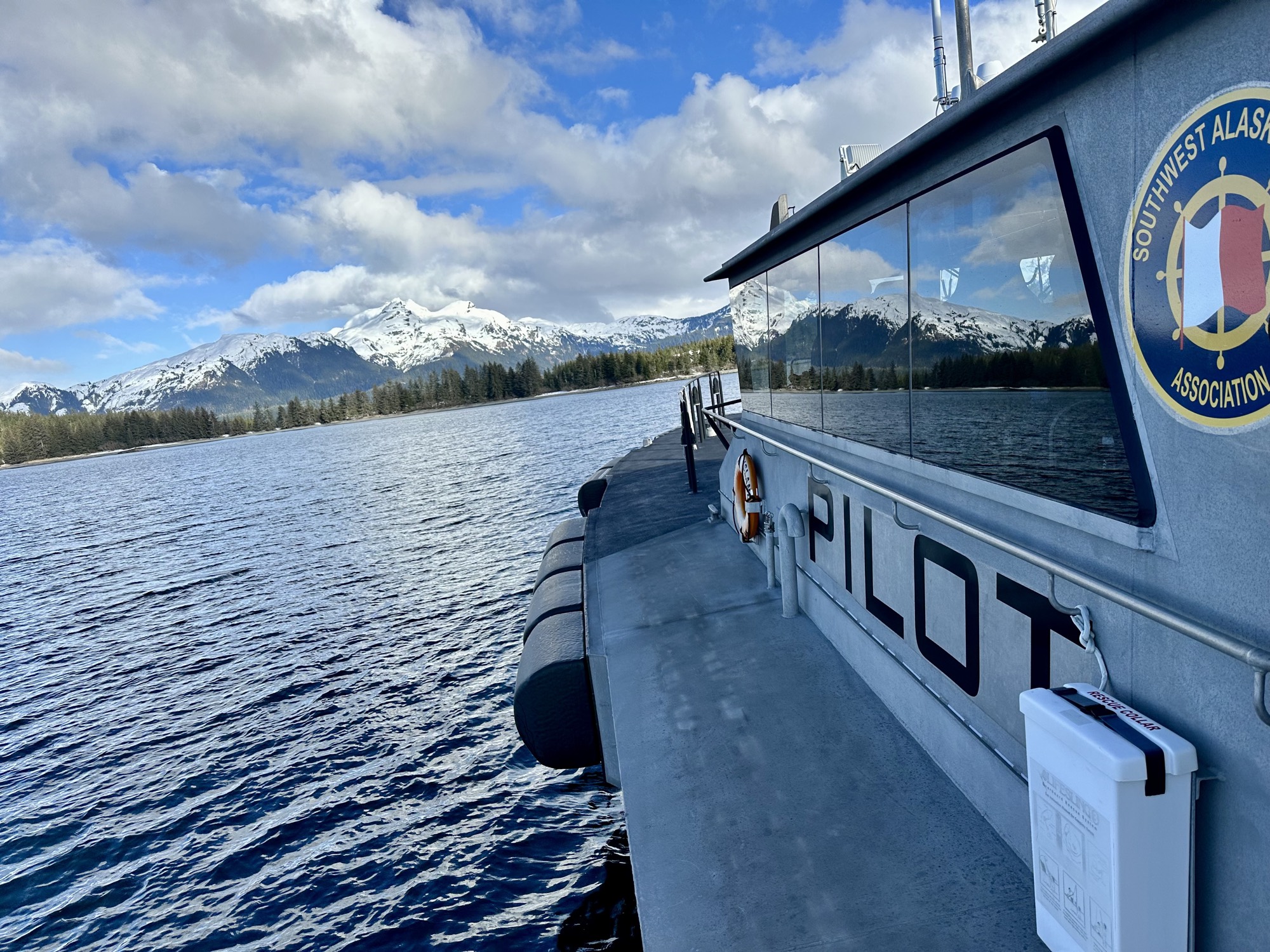 A SWAPA pilot boat underway, the association's roundel logo on the cabin, with snow-capped mountains behind
