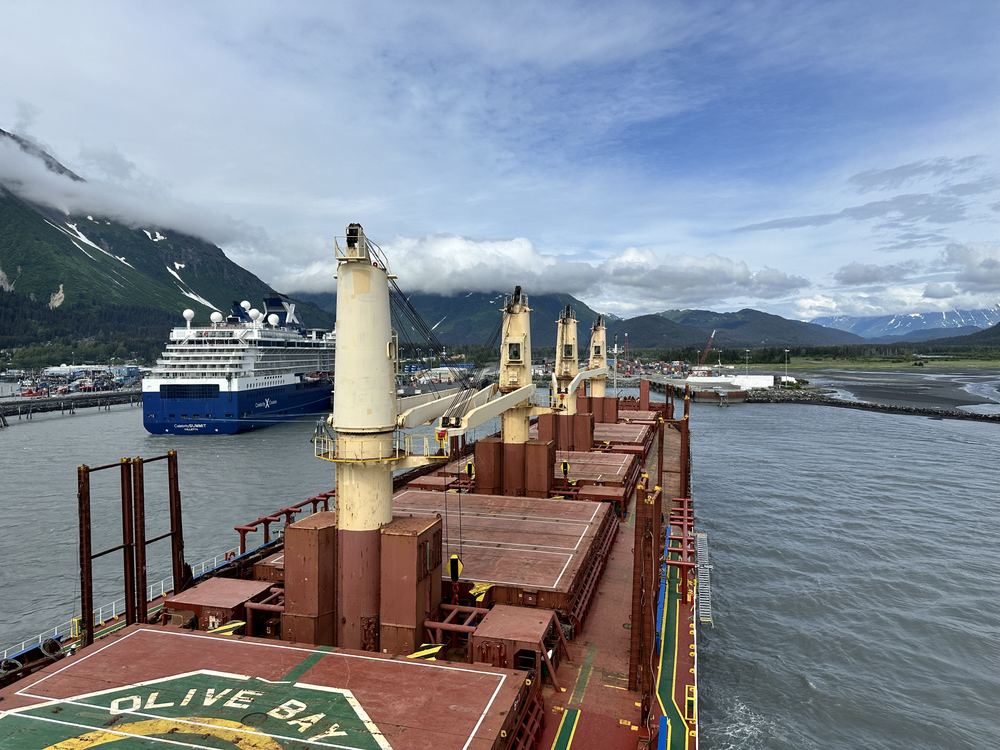 A bulk carrier's deck at Seward, with a cruise ship beyond